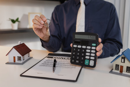 A businessman presents house models, keys, and contract documents, highlighting property investment and mortgage agreements, symbolizing home ownership, finance, and real estate success.の写真素材