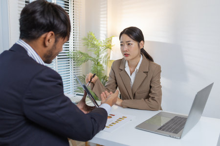 Two business professionals are discussing financial charts and strategies in a modern office. They exchange ideas, analyze reports, and negotiate solutions during a formal meeting.の写真素材