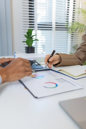 Business colleagues are engaged in a financial meeting, reviewing colorful charts and reports. They exchange ideas, make notes, and analyze strategies to achieve effective results.の写真素材