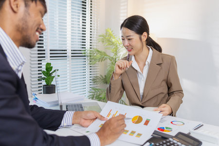 Business colleagues are engaged in a financial meeting, reviewing colorful charts and reports. They exchange ideas, make notes, and analyze strategies to achieve effective results.の写真素材