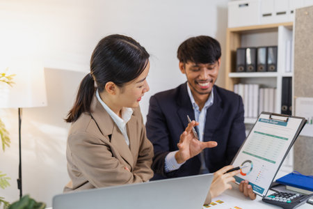 Two business professionals are discussing financial charts and reports in a modern office. They...