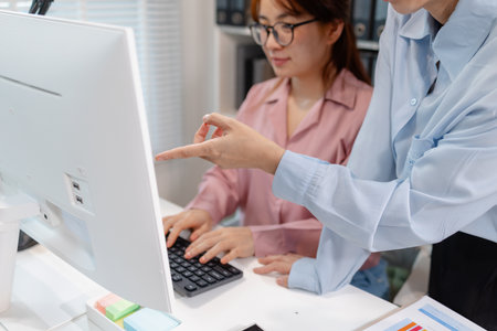 Two Asian office colleagues working together in the same department, reviewing documents and discussing project details during a team meeting, showing professional collaboration and teamwork.の写真素材