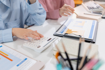 Two female colleagues discussing business reports together in a modern office environment, representing teamwork, data analysis, and collaboration in a start-up company setting.の写真素材