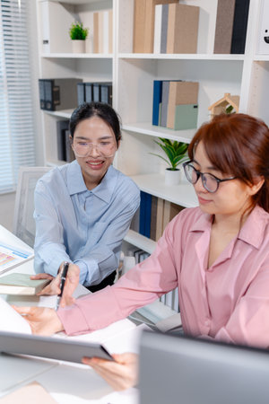 Two female colleagues discussing business reports together in a modern office environment, representing teamwork, data analysis, and collaboration in a start-up company setting.の写真素材