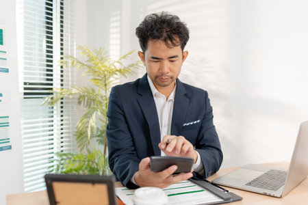 A businessman in a suit analyzing financial charts and performance reports in a bright modern office, focusing on strategy, data, and budget planning for company growth and long-term success.の写真素材