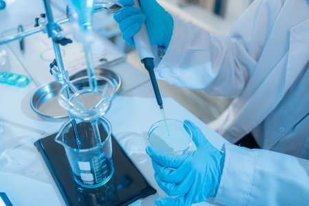 Two female scientists in white lab coats working together in a bright laboratory with microscopes, glassware, and blue test tubes, representing teamwork and modern scientific research environment.の写真素材