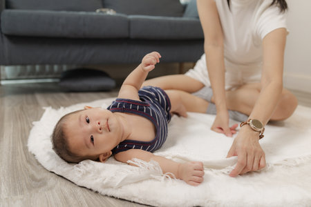 A loving mother spends quality time with her baby, helping him practice tummy time, rolling, and...