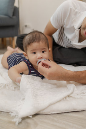 A father spends quality time with his baby, playing and bonding through gentle care and fun moments on a soft mat. The baby explores tummy time and pacifier use with support.の写真素材