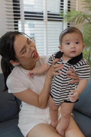 A young mother lovingly cradles her baby on a sofa, symbolizing maternal care, bonding, and...
