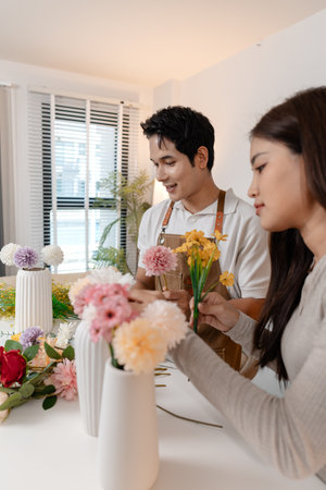 A young couple arranging colorful flowers together in a cozy home setting. The man, wearing an apron, helps the woman create a beautiful bouquet, sharing smiles and creativity in harmony.の写真素材