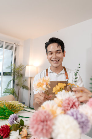 A young couple arranging colorful flowers together in a cozy home setting. The man, wearing an apron, helps the woman create a beautiful bouquet, sharing smiles and creativity in harmony.の写真素材