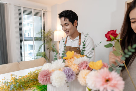 A young couple arranging colorful flowers together in a cozy home setting. The man, wearing an apron, helps the woman create a beautiful bouquet, sharing smiles and creativity in harmony.の写真素材