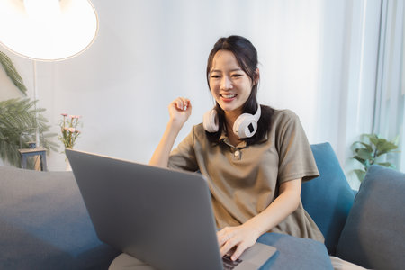 A young woman wearing headphones interacts with her laptop in different moods, from excitement to focus, showing modern lifestyle moments of gaming, learning, and online communication at home.の写真素材