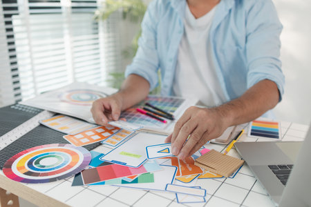 A designer is working on a creative UX UI project at a desk, arranging color palettes and layout templates with focus and precision, representing modern design and innovation.の写真素材