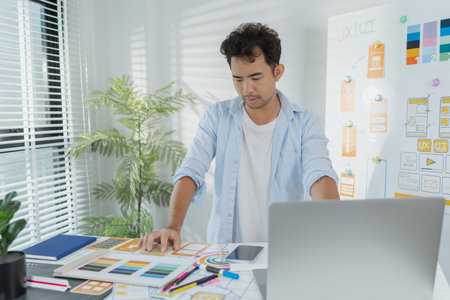 A creative designer works on UX/UI planning, analyzing sketches and prototypes on a whiteboard while...