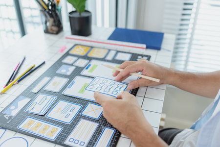 A designer is developing UX UI layouts, reviewing mobile app prototypes, and arranging interface...