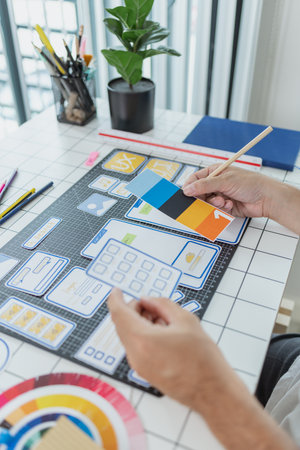 A male designer focused on UX UI tasks, creating app prototypes with wireframes, sketches, and color...