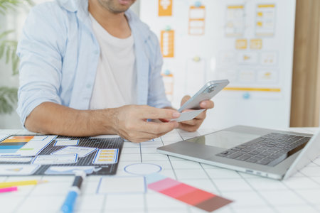 A male designer focused on UX UI tasks, creating app prototypes with wireframes, sketches, and color palettes. He works with creative ideas to optimize user interface and usability.の写真素材
