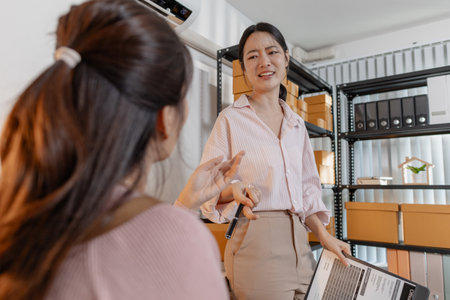 Two young women working together in a small business office, organizing packages, reviewing documents, and planning tasks with smiles. Scene reflects teamwork, productivity and modern entrepreneurshipの写真素材