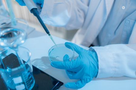 Two female scientists in white lab coats working together in a bright laboratory with microscopes,...