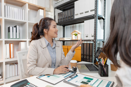 Two Asian businesswomen discussing company strategy together in a modern office, analyzing financial documents and charts. They are collaborating and sharing ideas for future business development.の写真素材