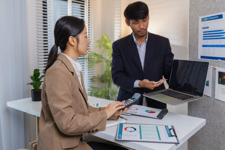 Business colleagues are engaged in a collaborative discussion, analyzing financial charts and reports on the wall and table. They exchange ideas, review strategies, and plan future goals.の写真素材