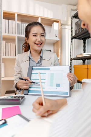 Two Asian businesswomen discussing ideas and analyzing reports from documents in a modern office. They collaborate on business strategies, teamwork, and organizational planning for success.の写真素材