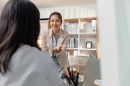 Two Asian businesswomen discussing company strategy together in a modern office, analyzing financial documents and charts. They are collaborating and sharing ideas for future business development.の写真素材