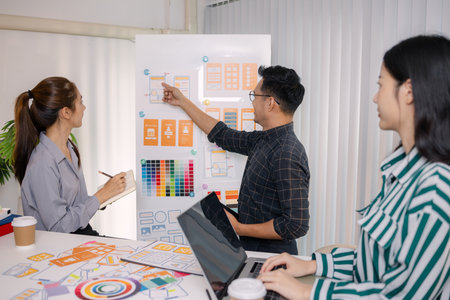 UX/UI designers collaborating during a creative workshop to test interface ideas and exchange feedback for app development, emphasizing teamwork and innovative design thinking.の写真素材