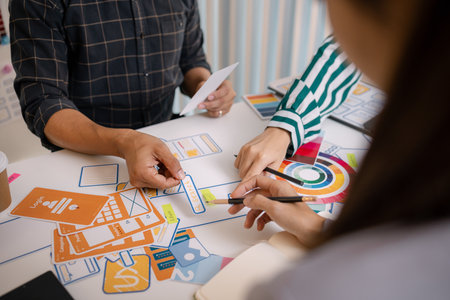 A group of UX/UI designers brainstorming creative ideas together, discussing color palettes and layout concepts for a new mobile application interface in a modern design office.の写真素材