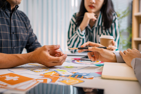 Designers having a UX/UI planning meeting to refine mobile app layouts and user flow. They...
