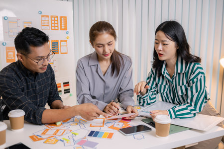 Designers having a UX/UI planning meeting to refine mobile app layouts and user flow. They collaborate closely to create functional and visually appealing interface solutions.の写真素材