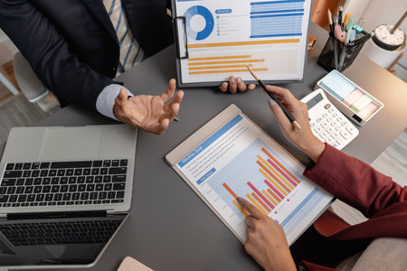 Business professionals reviewing financial charts and performance reports during a meeting, highlighting strategic planning, budget analysis, and teamwork in a modern corporate environment.の写真素材
