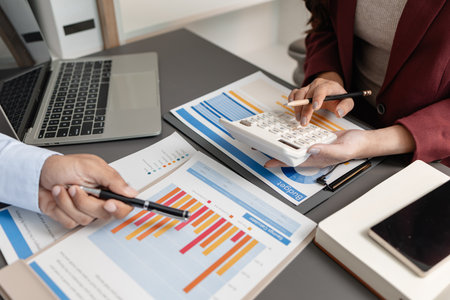 Business professionals meeting at a modern office table, reviewing charts and budget reports while discussing key financial insights and strategic plans for upcoming business decisions.の写真素材