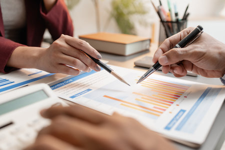 A business meeting scene where professionals review financial charts and exchange insights, highlighting strategic planning and collaborative decision making in a modern office environment.の写真素材