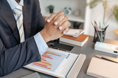Businessman working at a modern office desk, surrounded by documents, charts, and a laptop, creating a professional corporate environment suitable for finance, planning, and management themes.の写真素材