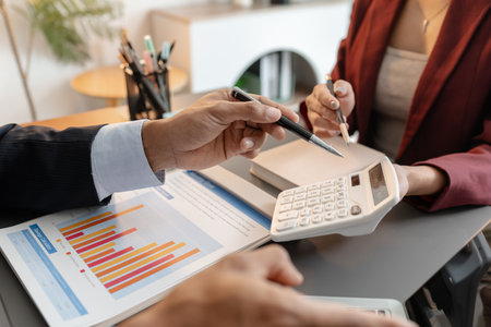 A collaborative startup meeting showing professionals reviewing financial charts and discussing strategic ideas in a modern office setting.の写真素材