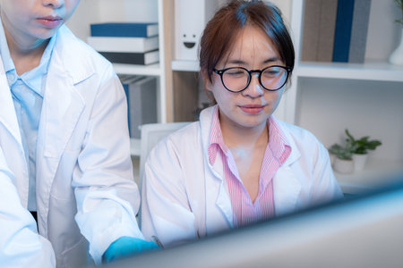 Two chemists in white lab coats working together in a modern laboratory surrounded by scientific equipment, computers, and glassware, representing teamwork in scientific research.の写真素材