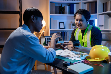 Architects and engineers work together in an office to review blueprints, exchange ideas, and refine their building plans for a contemporary construction project in an urban setting.の写真素材