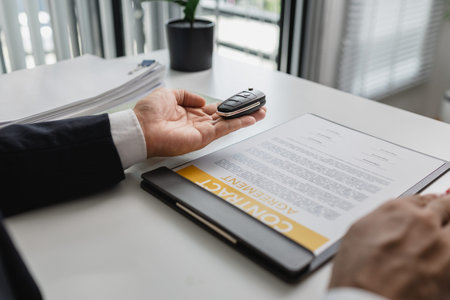 A businessman in a suit is presenting car insurance and contract documents with miniature car models...