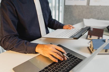 Contract documents, house models, keys, and calculator on the desk symbolize mortgage approval,...