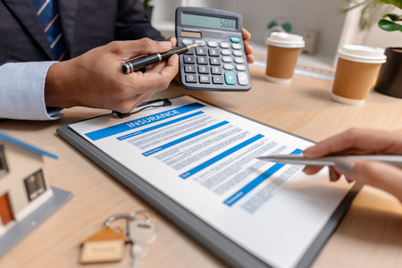 A real estate agent and client discussing property sale details at the office table, reviewing and...