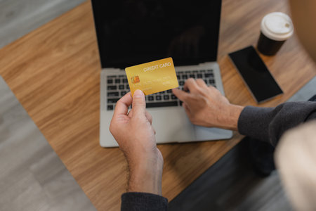 Man holding credit card while using laptop for online payment and digital shopping, representing...
