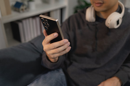 Man using smartphone while relaxing on sofa at home, browsing mobile apps and digital content,...