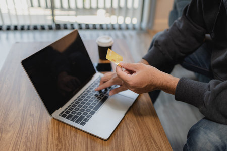 Man holding credit card while using laptop for online payment and digital shopping, representing...