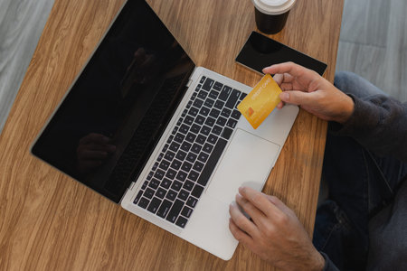 Man holding credit card while using laptop for online payment and digital shopping, representing...