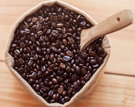 Coffee beans in sack with wooden scoop on top viewの写真素材