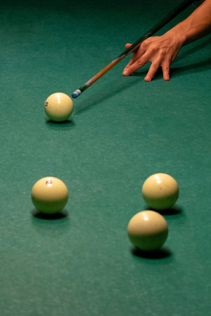 The arm of the Billiards player preparing to strike. Ivory white billiard balls on a green pool table. Russian billiards. Vertical photography.の写真素材