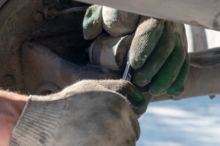 Hands in defense gloves mechanics to repair the suspension on the car. Work with a wrench. Self-repair of the car. Replacing the shock absorber strut.の写真素材