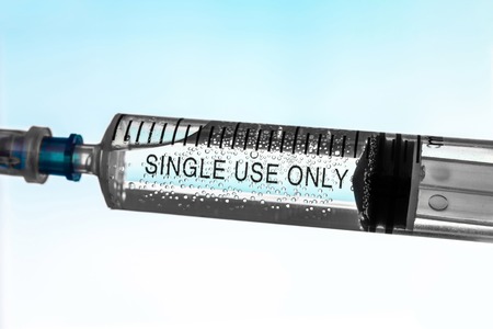 Close-up syringe filled with liquid with air bubbles. Inscription - single use only. White and blue background. Prevention of the spread of infectious diseases. Concept medical waste disposal.の写真素材